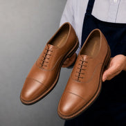 Man holding a pair of Melodiapelle Mount Pleasant Oxford shoes in tan leather, close-up