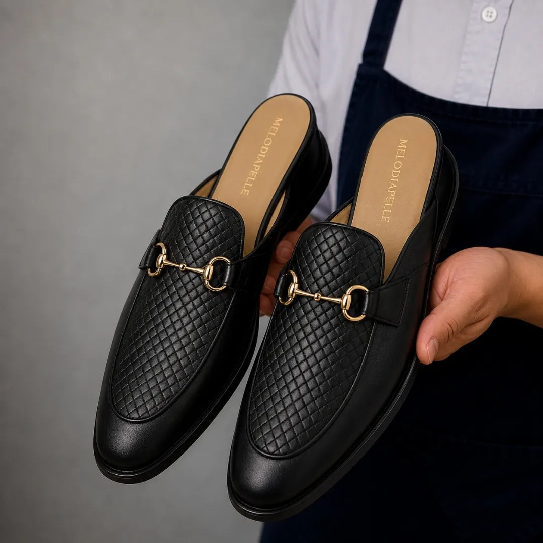 Man holding a pair of Melodiapelle Munar Mule shoes in black woven leather, close-up