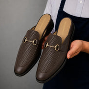 Man holding a pair of Melodiapelle Munar Mule shoes in dark brown woven leather, close-up