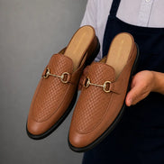 Man holding a pair of Melodiapelle Munar Mule shoes in tan woven leather, close-up