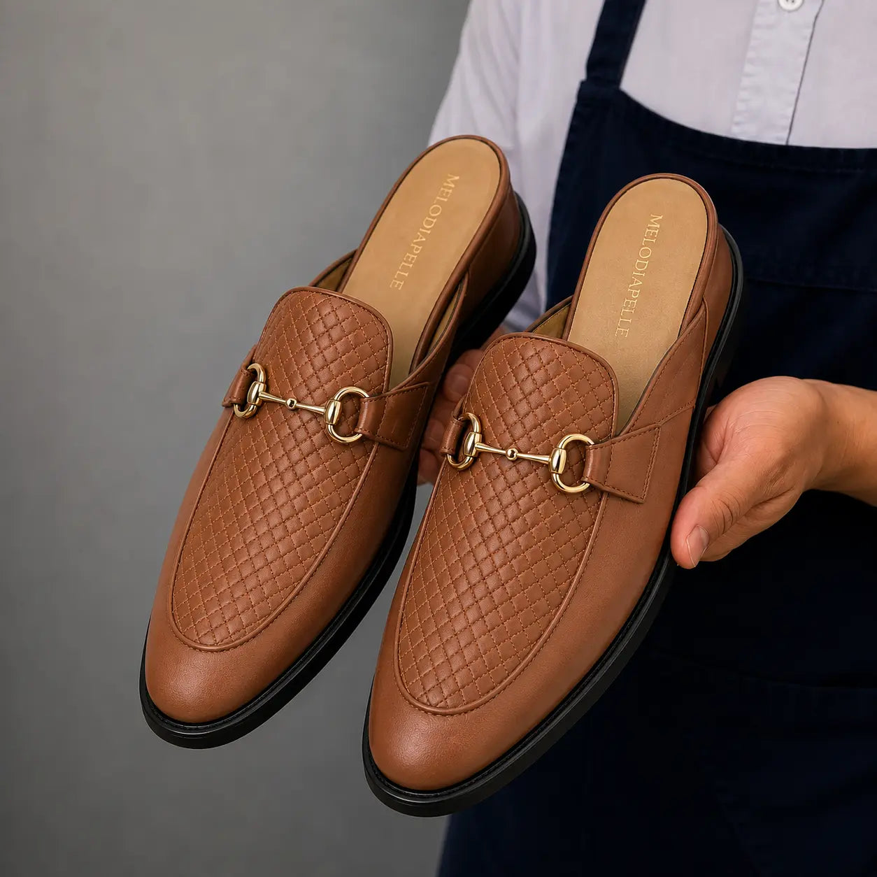 Man holding a pair of Melodiapelle Munar Mule shoes in tan woven leather, close-up