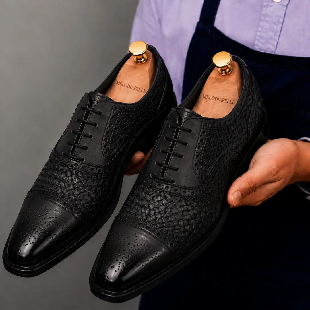 Man holding a pair of Melodiapelle Munich Woven Brogue Oxford shoes in black leather, close-up