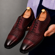 Man holding a pair of Melodiapelle Munich Woven Brogue Oxford shoes in bordeaux leather, close-up