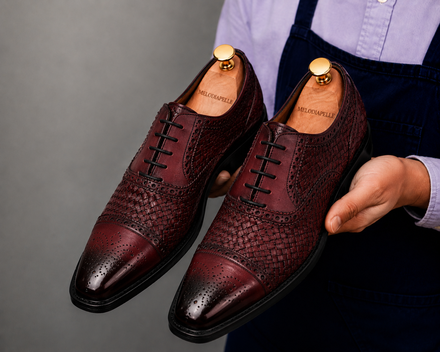 Man holding a pair of Melodiapelle Munich Woven Brogue Oxford shoes in bordeaux leather, close-up