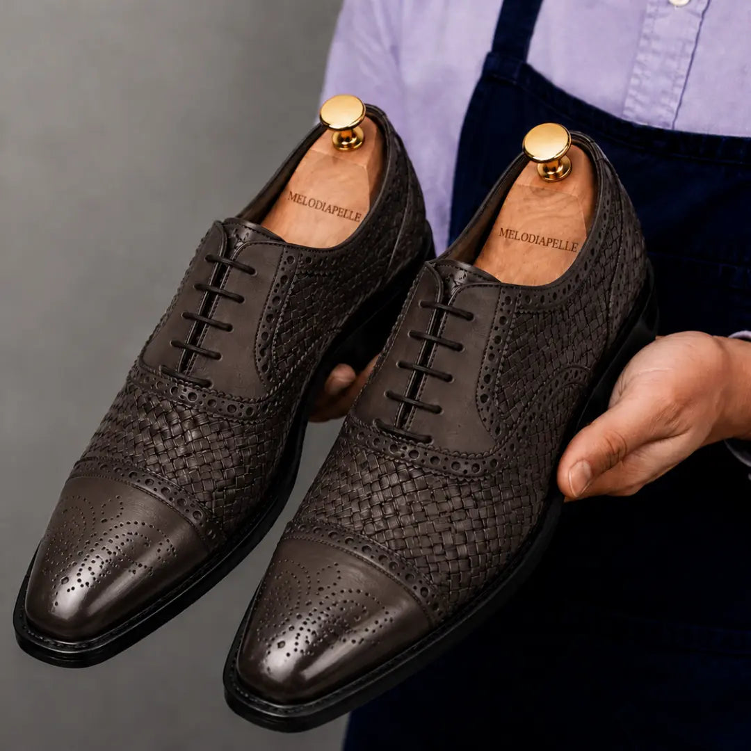 Man holding a pair of Melodiapelle Munich Woven Brogue Oxford shoes in brown leather, close-up
