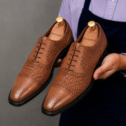 Man holding a pair of Melodiapelle Munich Woven Brogue Oxford shoes in tan leather, close-up