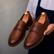 Man holding a pair of Melodiapelle Mustang Croc-Penny Loafer shoes in dark chocolate leather, close-up