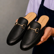 Man holding a pair of Melodiapelle Mustang Mules in black leather, close-up