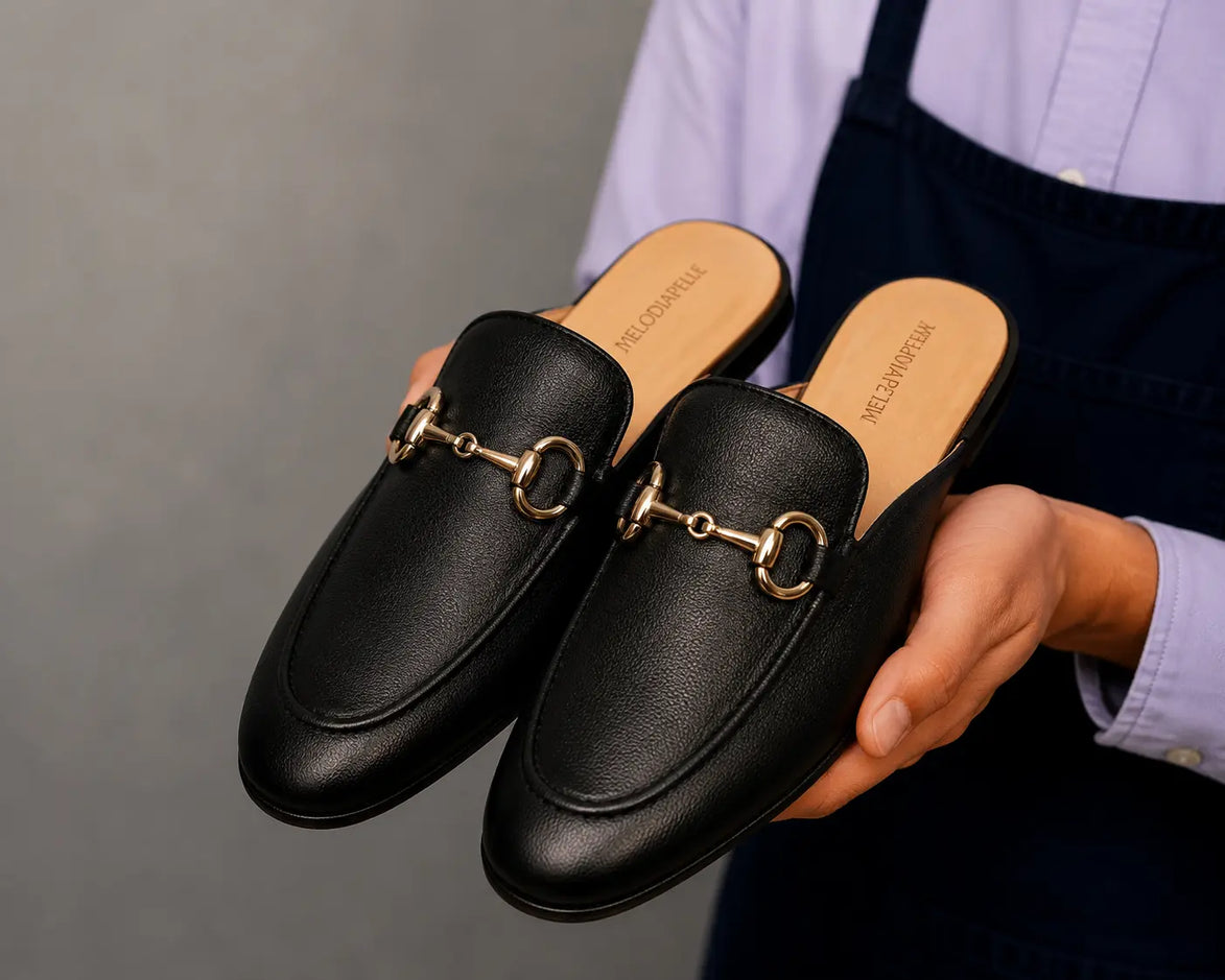 Man holding a pair of Melodiapelle Mustang Mules in black leather, close-up