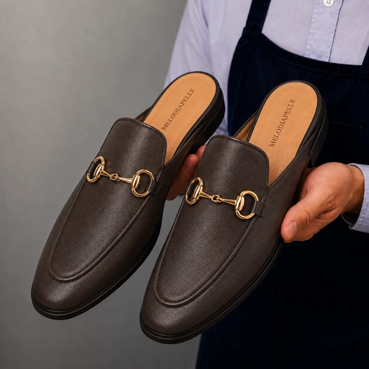 Man holding a pair of Melodiapelle Mustang Mules in dark brown leather, close-up