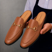 Man holding a pair of Melodiapelle Mustang Mules in tan leather, close-up