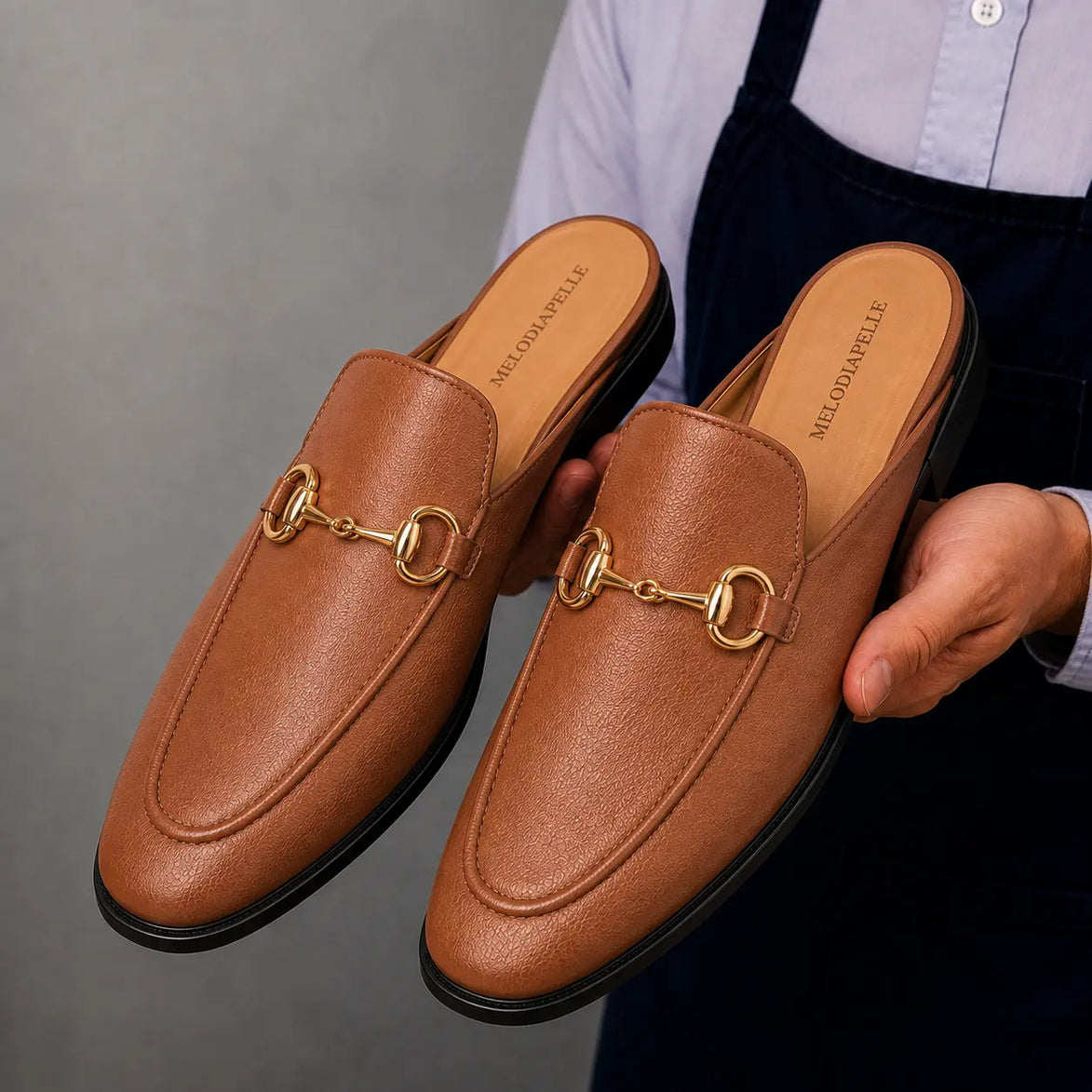 Man holding a pair of Melodiapelle Mustang Mules in tan leather, close-up