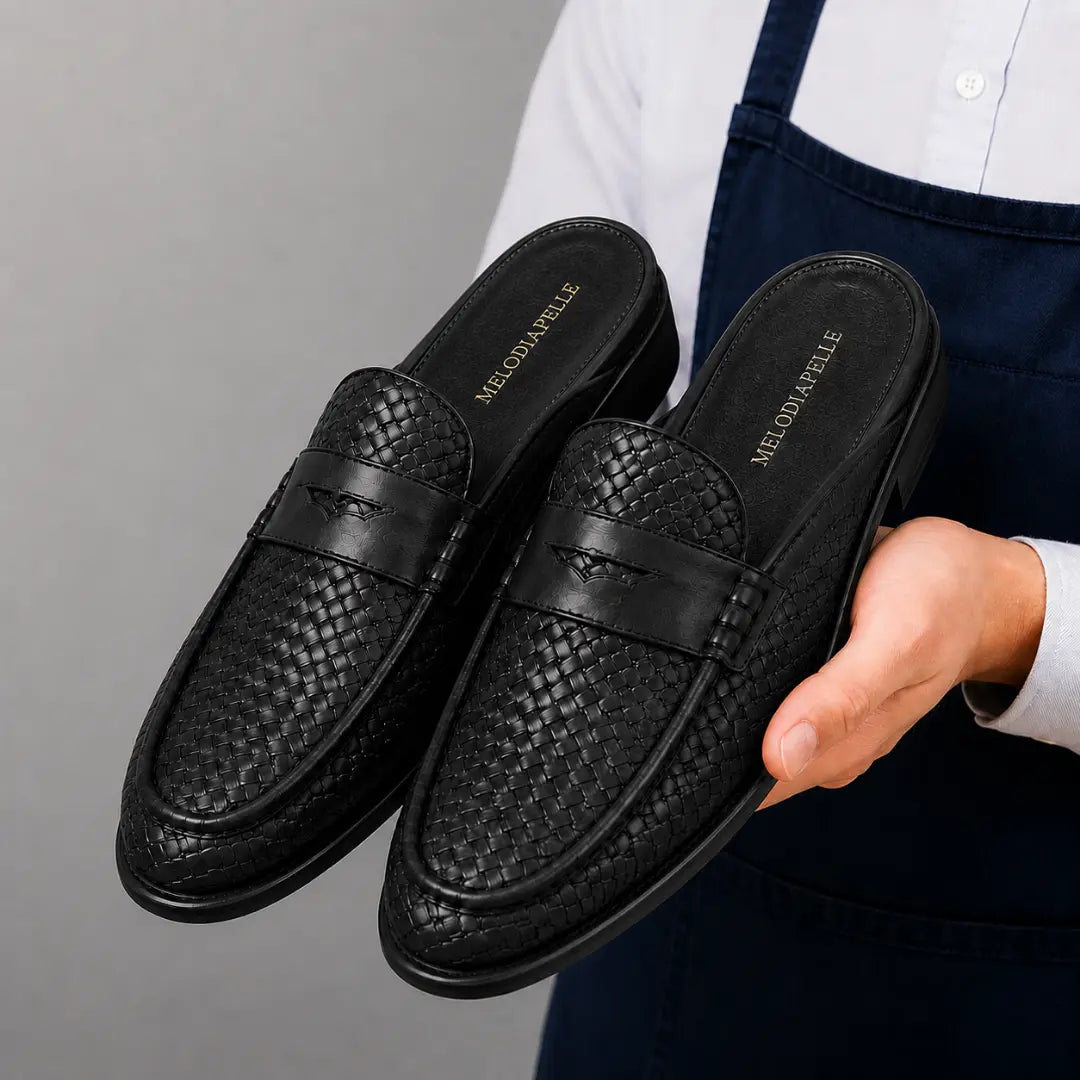 Man holding a pair of Melodiapelle Rossi Mule shoes in black woven leather, close-up