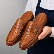 Man holding a pair of Melodiapelle Rossi Mule shoes in cognac tan woven leather, close-up