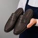 Man holding a pair of Melodiapelle Rossi Mule shoes in dark brown woven leather, close-up