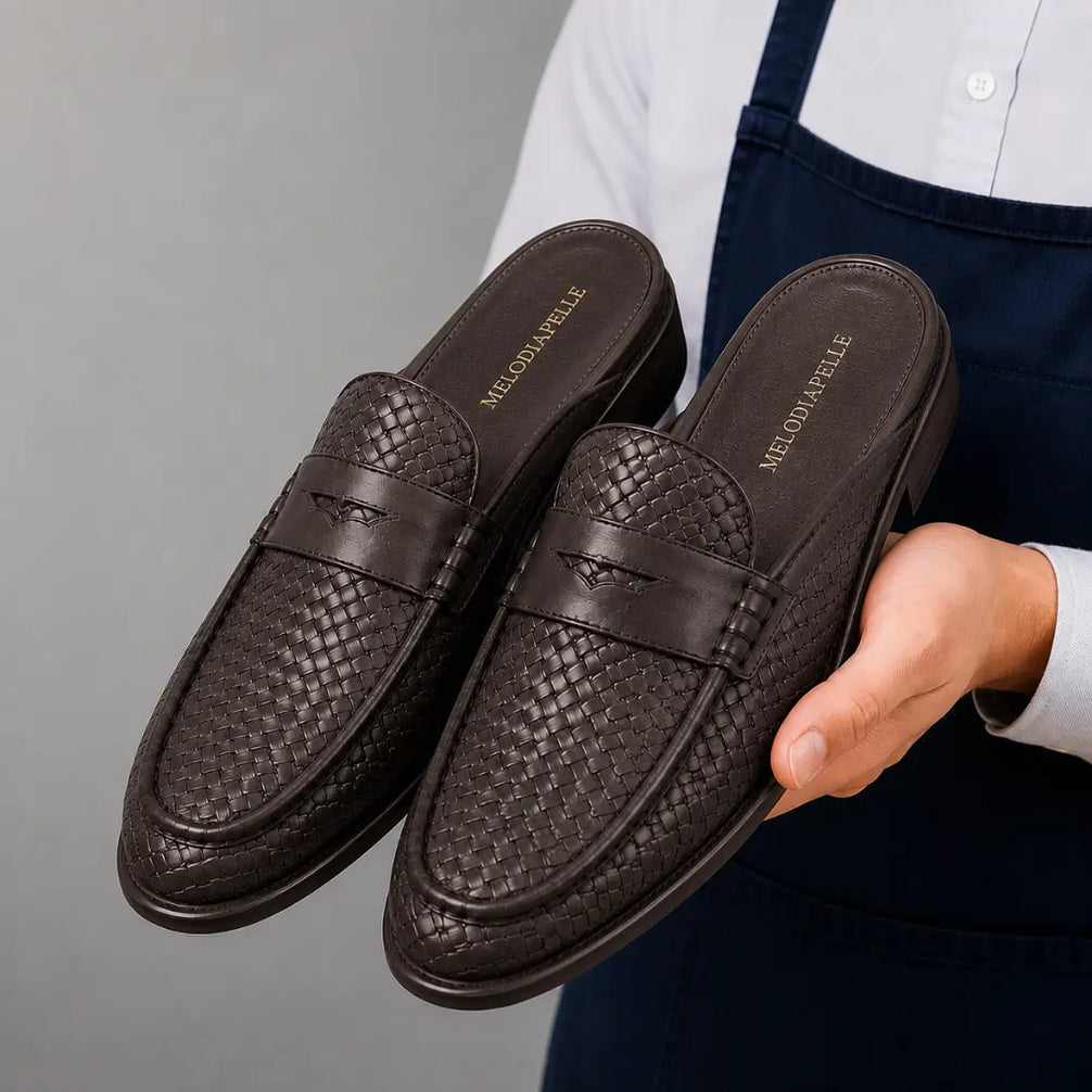 Man holding a pair of Melodiapelle Rossi Mule shoes in dark brown woven leather, close-up