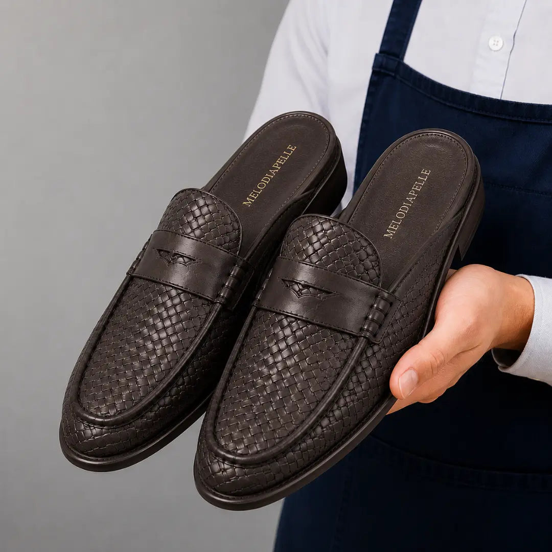 Man holding a pair of Melodiapelle Rossi Mule shoes in dark brown woven leather, close-up