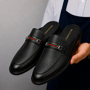 Man holding a pair of Melodiapelle Sergio Mule shoes in black leather, close-up