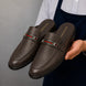 Man holding a pair of Melodiapelle Sergio Mule shoes in dark brown leather, close-up