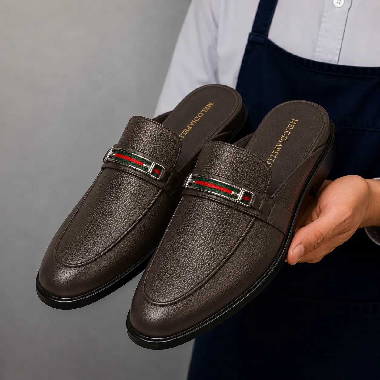 Man holding a pair of Melodiapelle Sergio Mule shoes in dark brown leather, close-up