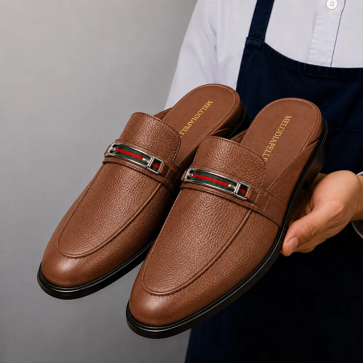 Man holding a pair of Melodiapelle Sergio Mule shoes in tan leather, close-up